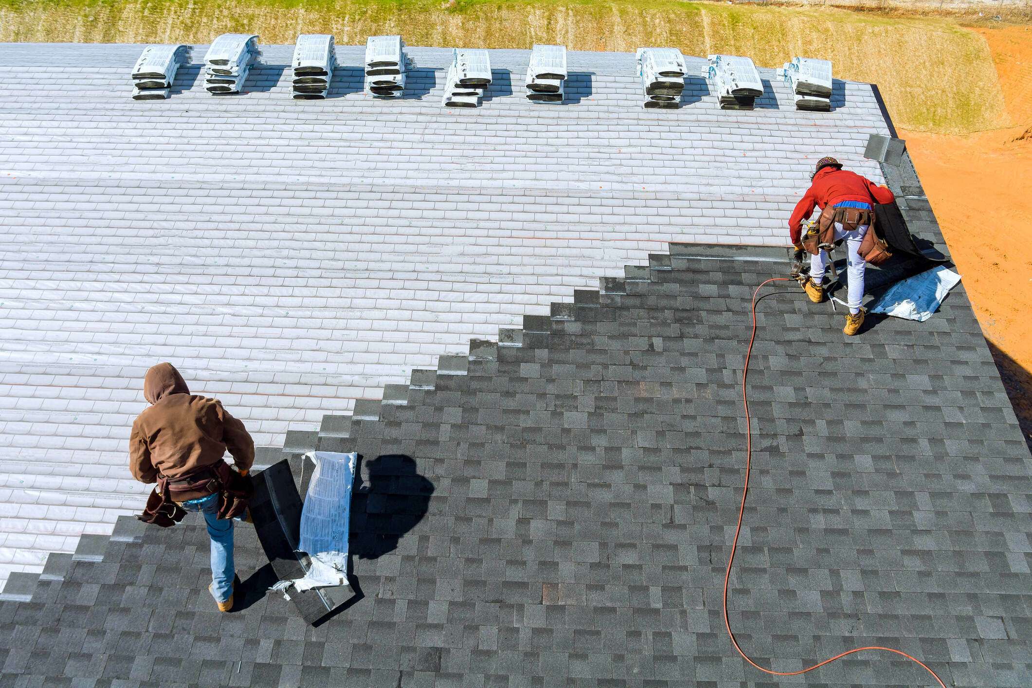Aerial view of workers installing residential roofing shingles with air hammer and nail